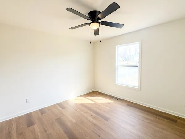 an empty room with wooden floor ceiling fan and windows