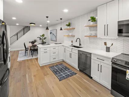 a large kitchen with stainless steel appliances granite countertop a stove top oven a sink dishwasher and white cabinets with wooden floor