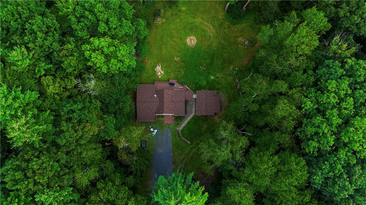 A secluded aerial view highlights a private residence enveloped by a dense canopy of mature trees.