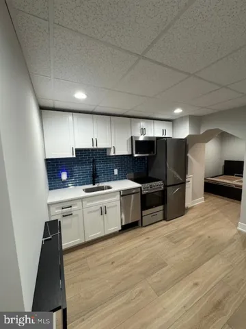 a kitchen with stainless steel appliances granite countertop a sink a stove a refrigerator with white cabinets and wooden floor