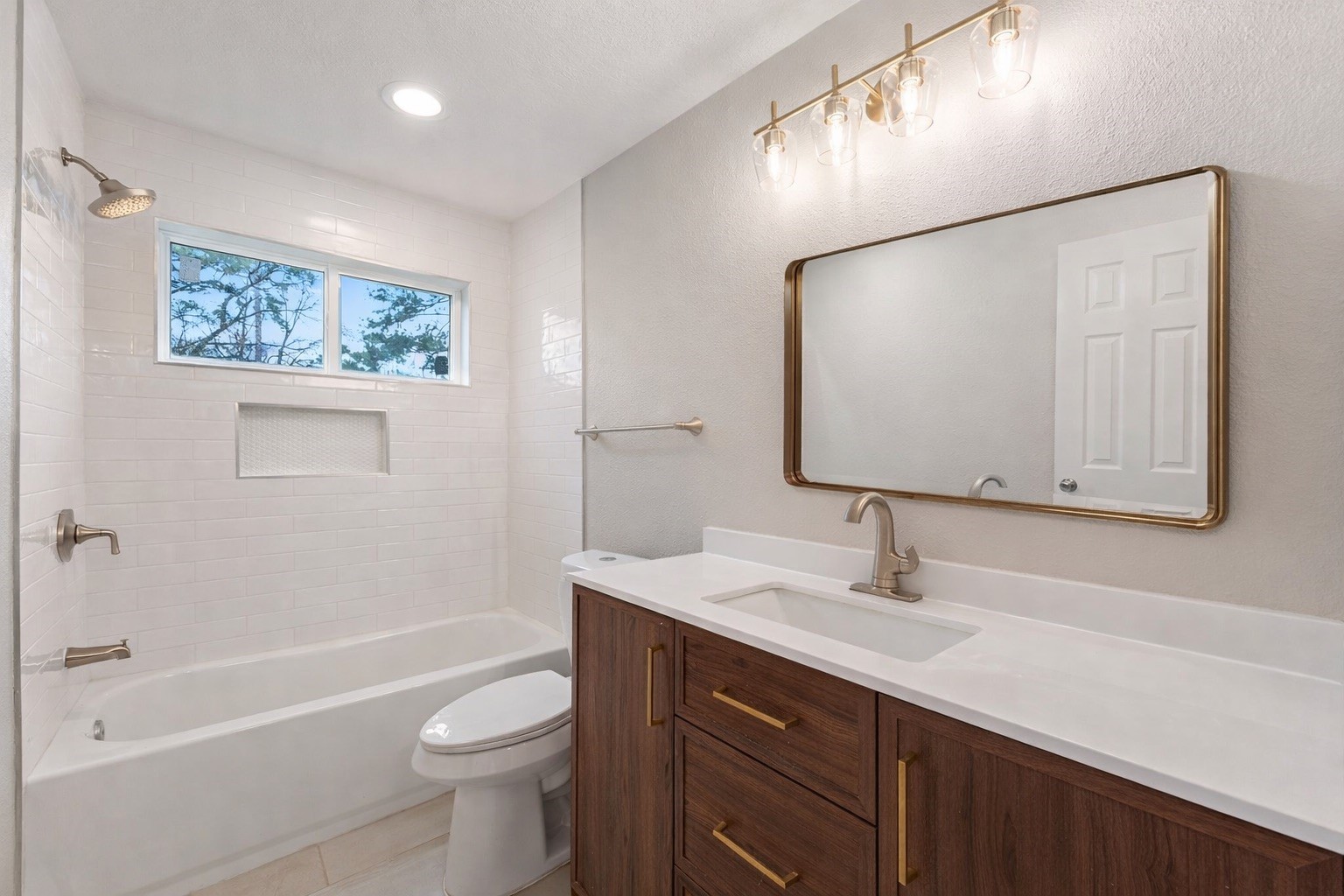 19711 Bishops Gate Lane Humble, TX 77338 - Photo 9 of 12 Fully updated secondary bath featuring a modern vanity with warm brass accents, a clean quartz countertop, and a classic tiled tub-shower combo with built-in niche. Bright, fresh, and ready for everyday use or guests.