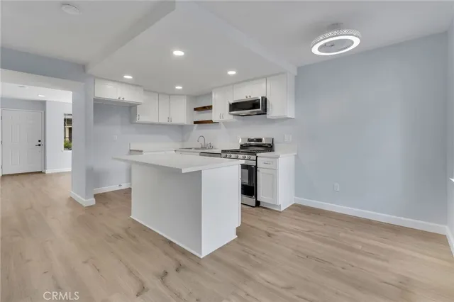 a kitchen with stainless steel appliances granite countertop a stove top oven a sink dishwasher and a refrigerator with wooden floor