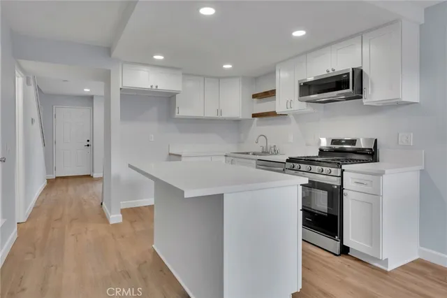 a kitchen with stainless steel appliances granite countertop a stove top oven a sink a refrigerator and white cabinets with wooden floor