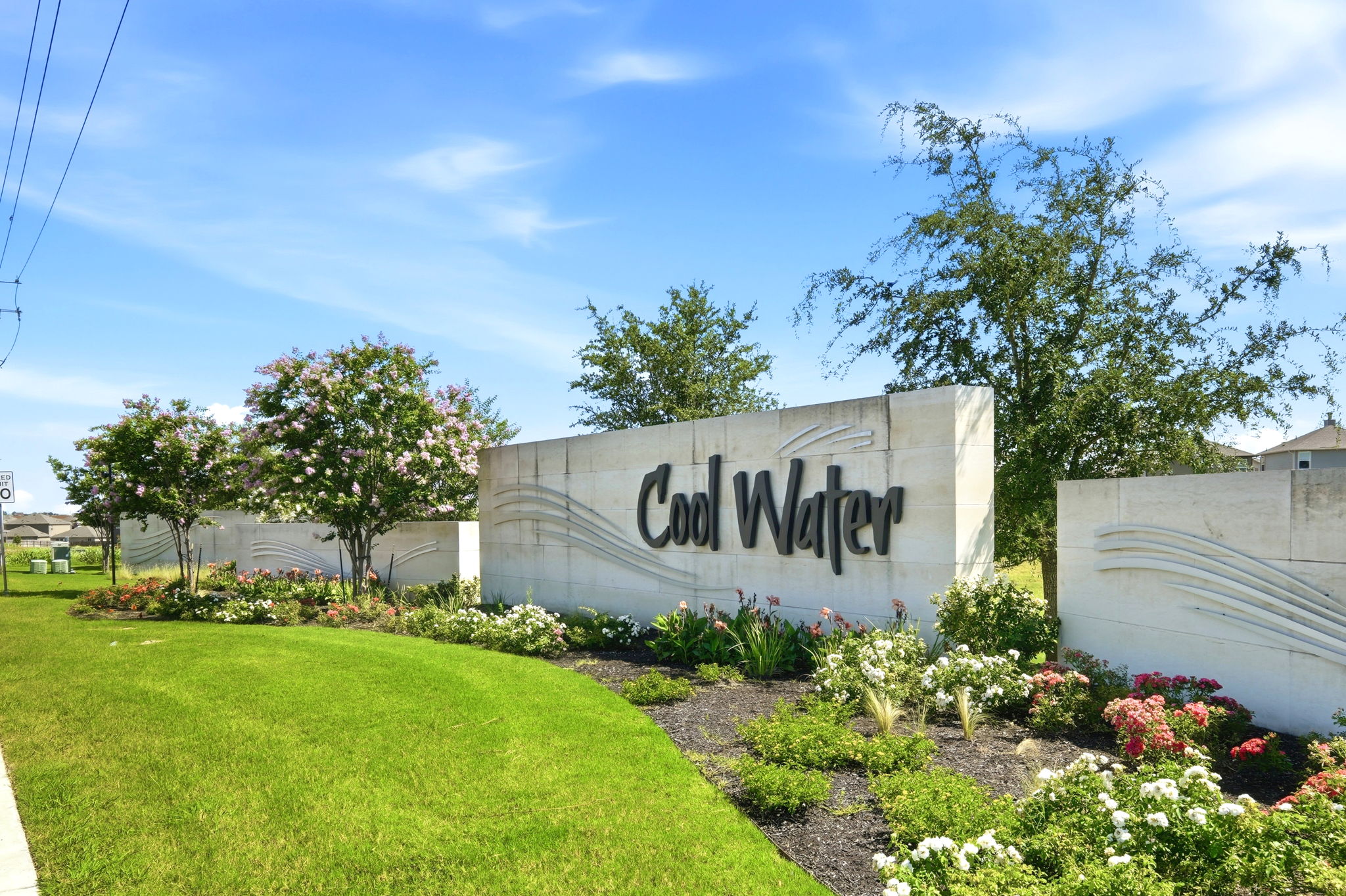 220 Lucky Texan Road Jarrell, TX 76537 - Photo 2 of 19 A vibrant entrance to the Cool Water community, framed by lush landscaping and a bright blue sky.