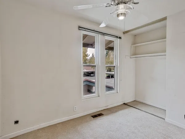 an empty room with a chandelier fan and windows