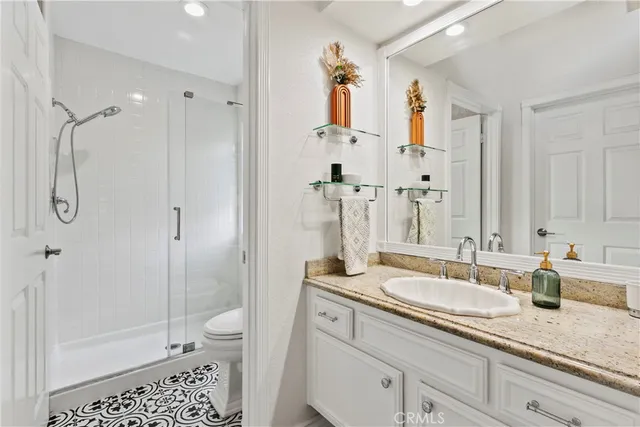 a bathroom with a granite countertop sink a toilet a mirror and shower