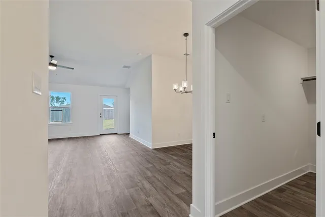 an empty room with wooden floor chandelier fan and windows