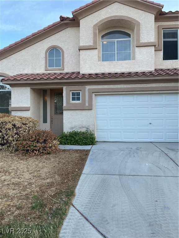 Townhome / multi-family property with a tile roof, driveway, a garage, and stucco siding