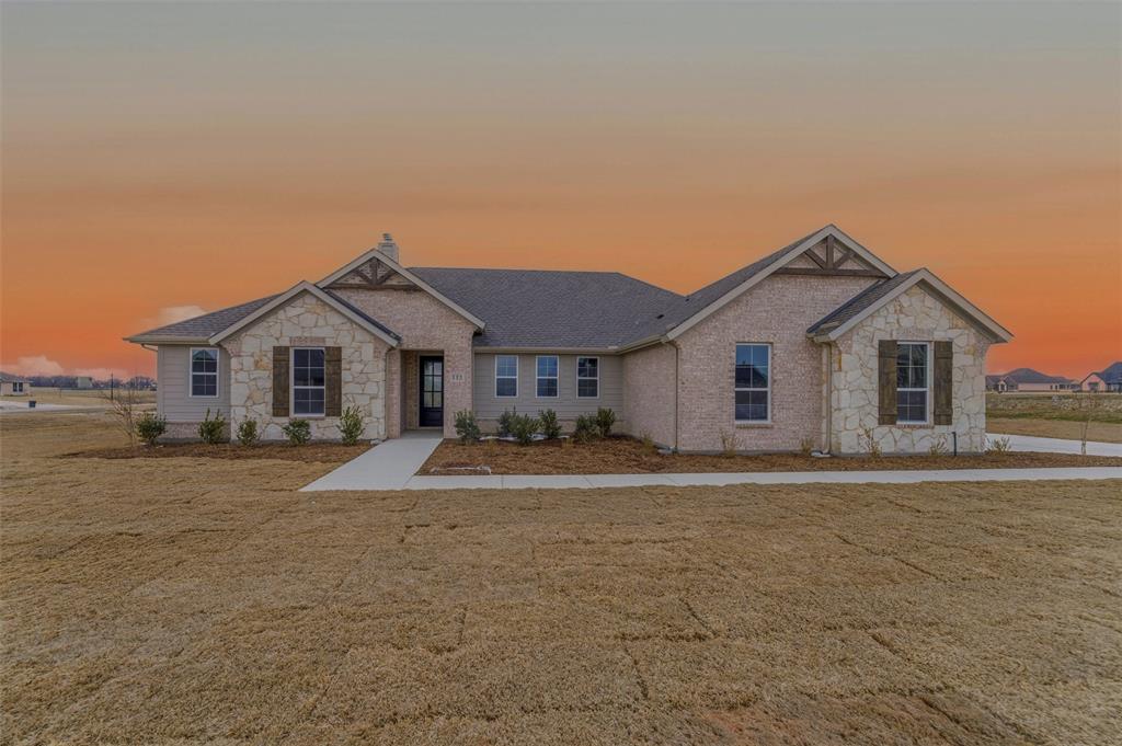 View of front of home with stone siding, a front yard, a chimney, and brick siding