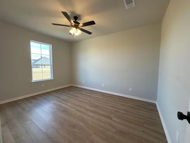 an empty room with wooden floor fan and windows