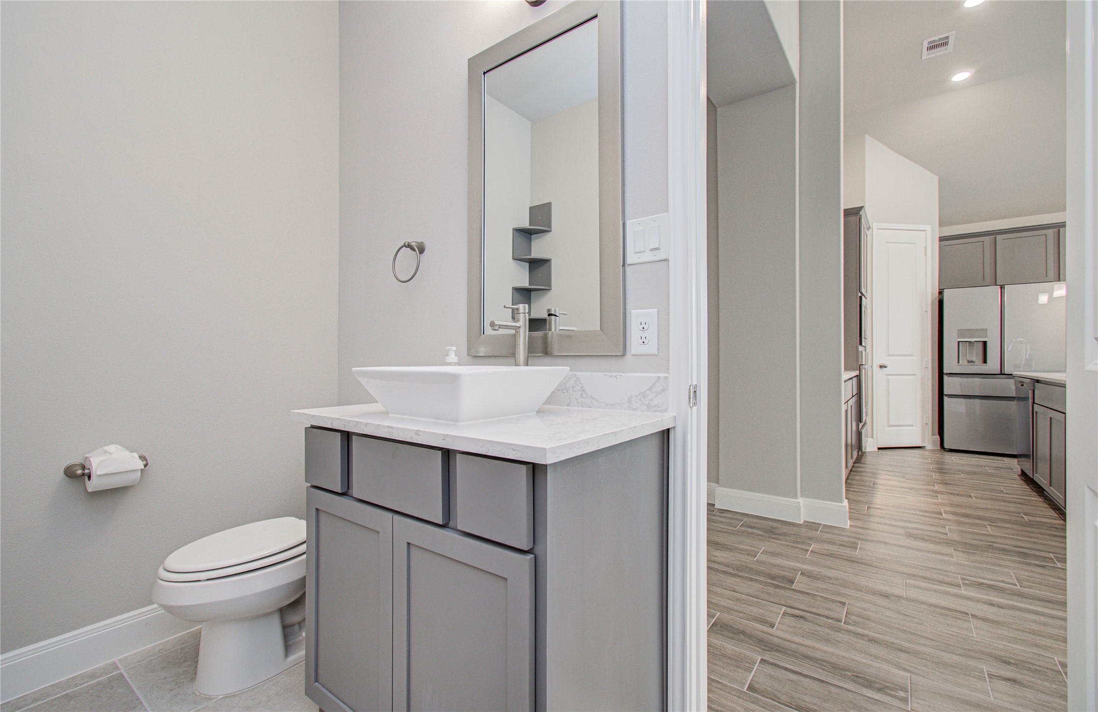 17344 Grand Canyon Road Conroe, TX 77302 - Photo 13 of 49 This modern home features a sleek bathroom with a vessel sink and gray cabinetry. Adjacent is a spacious kitchen with stainless steel appliances and contemporary tile flooring, offering a cohesive and stylish aesthetic.