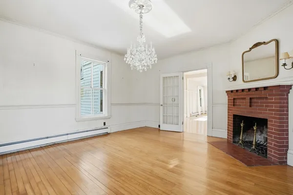 a view of an empty room with wooden floor fireplace and a window