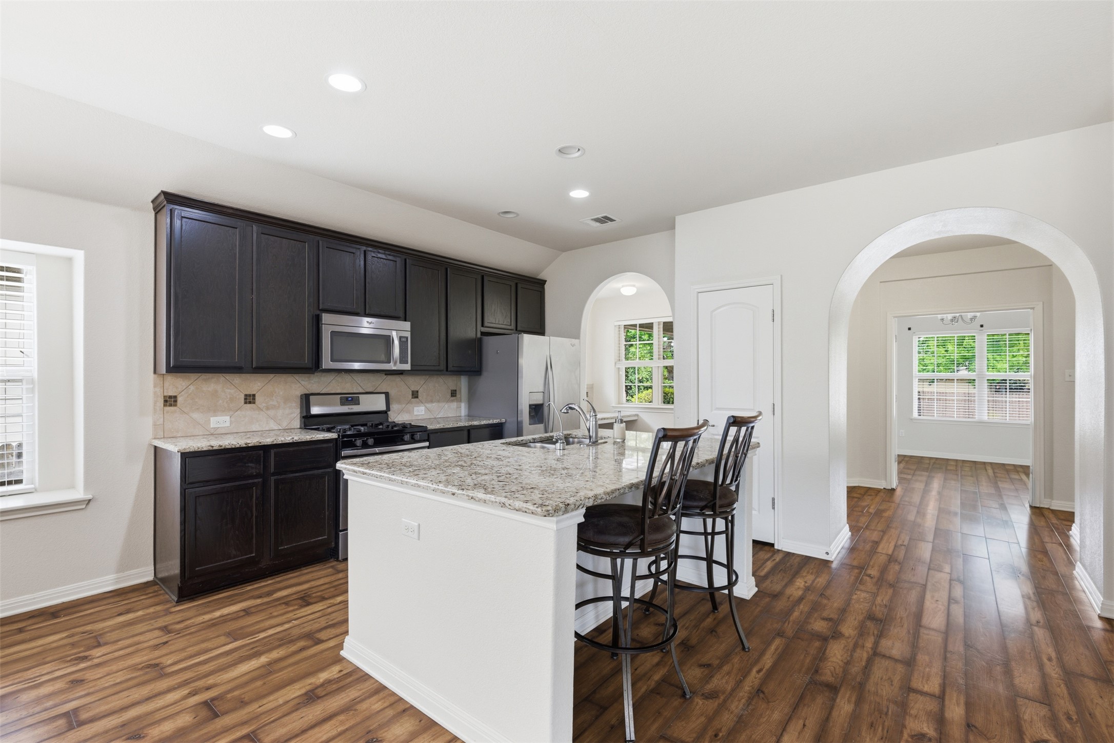 339 Sycamore Street Georgetown, TX 78633 - Photo 10 of 28 Kitchen featuring a breakfast bar, an island with sink, stainless steel appliances, light stone counters, and dark wood-style floors