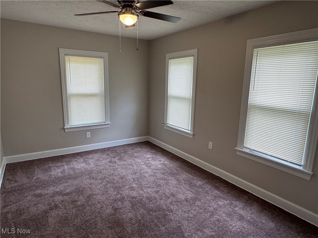 Unfurnished room with dark carpet, a textured ceiling, and ceiling​​‌​​​​‌​​‌‌​‌‌​​‌​​​​‌​​​‌‌​‌‌‌ fan