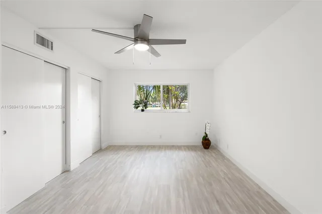 an empty room with wooden floor a ceiling fan and windows
