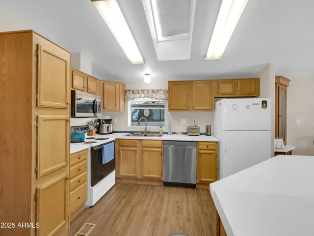 a kitchen with granite countertop a refrigerator a sink dishwasher a stove top oven a refrigerator and white cabinets with wooden floor