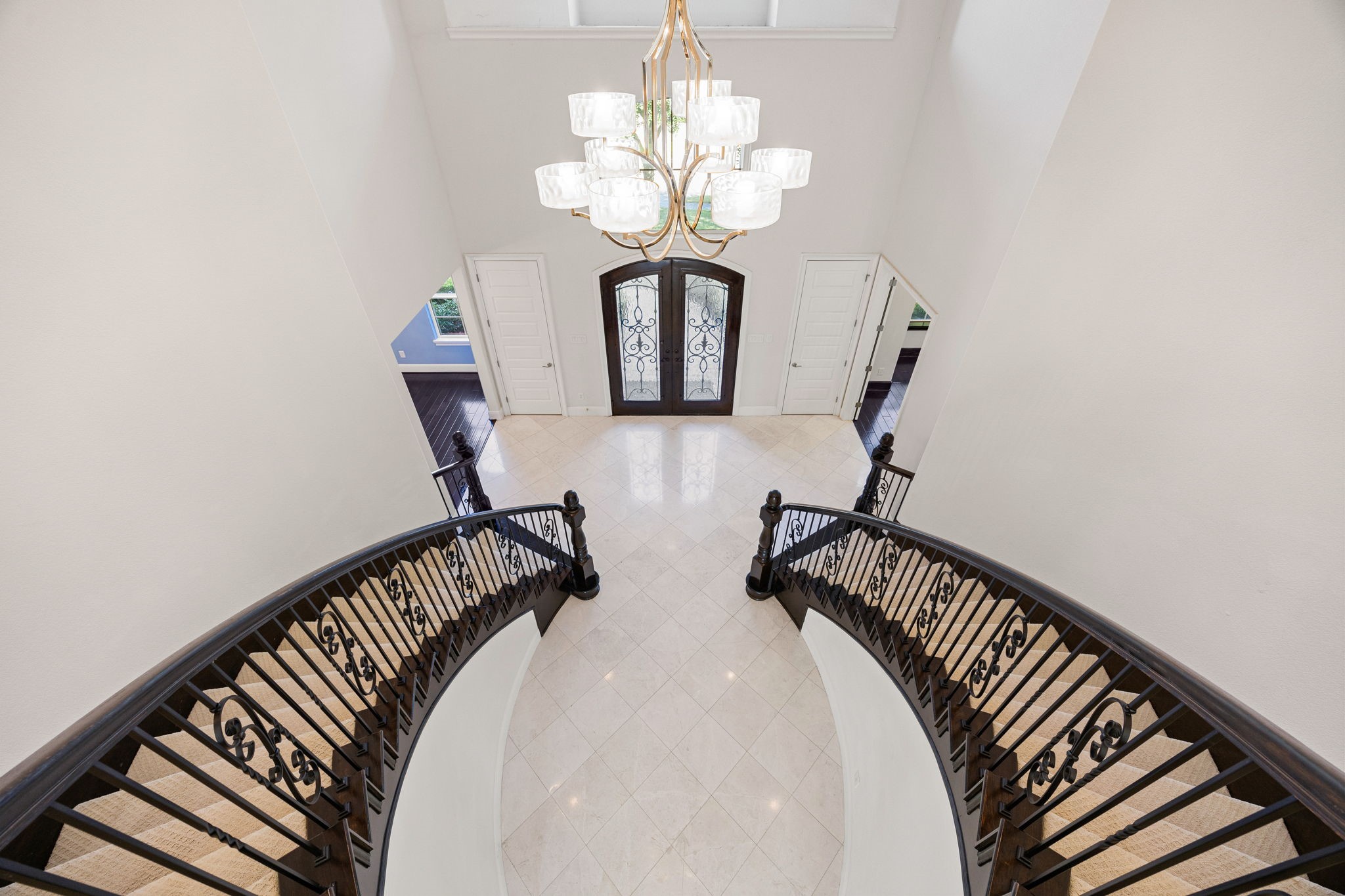 2102 Granite Brook Lane Katy, TX 77494 - Photo 23 of 39 A breathtaking view from the second floor showcases the grand dual staircase and elegant chandelier, highlighting the home’s stunning two-story entryway with custom wrought-iron doors and polished tile flooring.