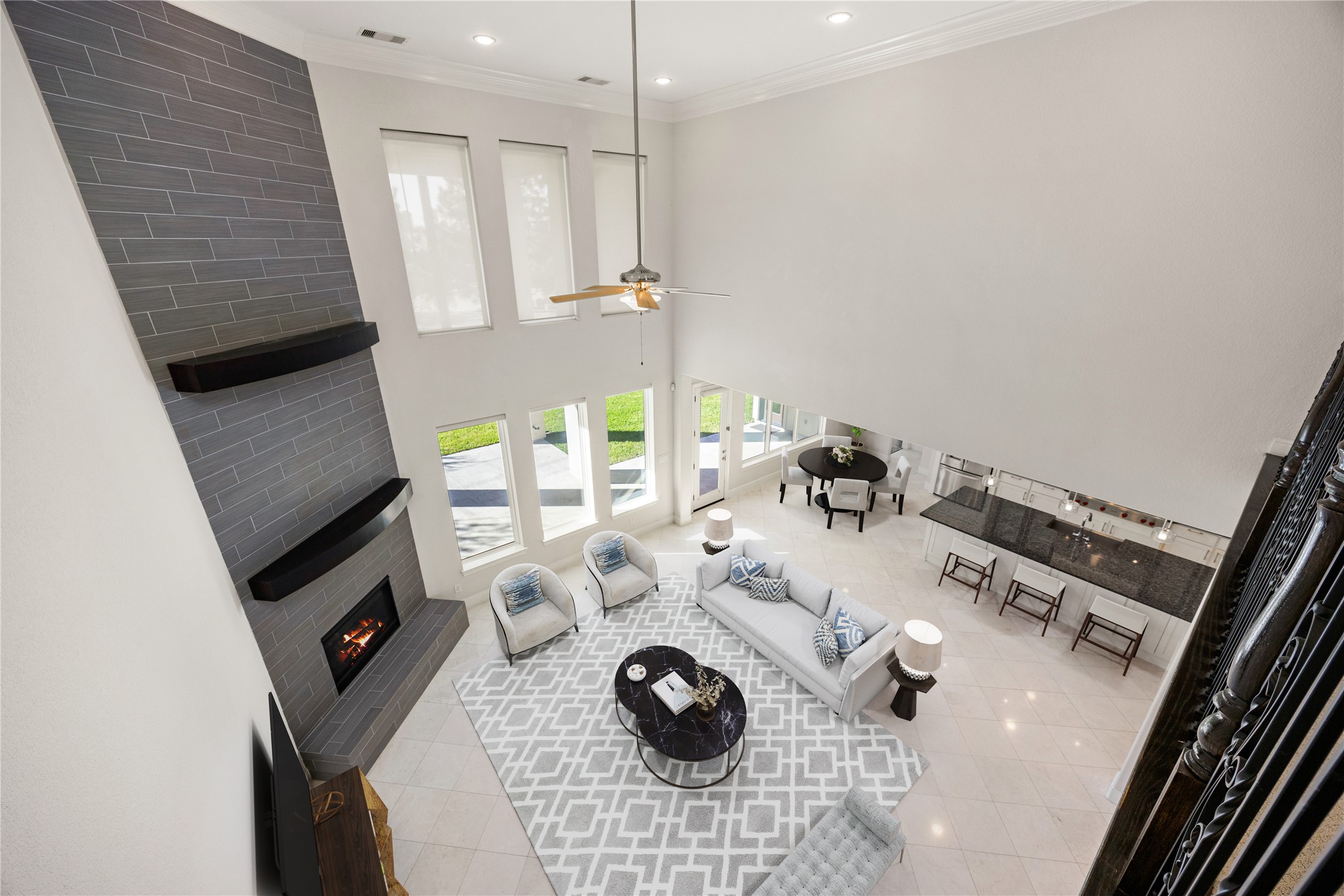 2102 Granite Brook Lane Katy, TX 77494 - Photo 24 of 39 An impressive view from above showcases the expansive family room with soaring ceilings, a sleek floor-to-ceiling tile fireplace, and a wall of windows offering abundant natural light and seamless views of the backyard and kitchen area. *Virtually Staged