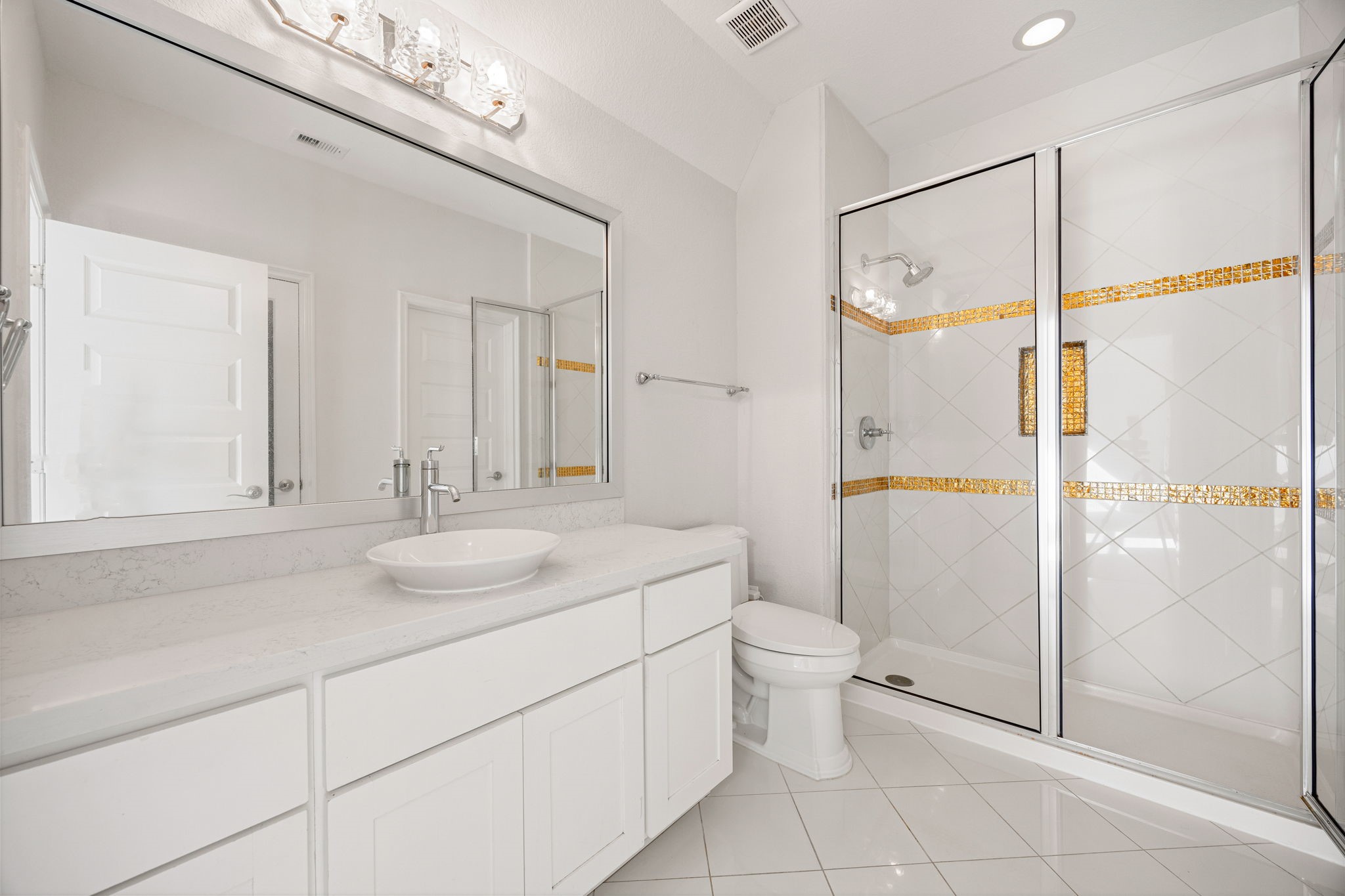 2102 Granite Brook Lane Katy, TX 77494 - Photo 33 of 39 This elegant secondary bath features a walk-in shower with stunning gold tile accents, modern fixtures, a sleek vessel sink, and a spacious vanity with ample storage.