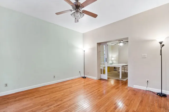 an empty room with wooden floor chandelier fan and windows