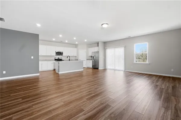 a view of an empty room with wooden floor kitchen view and a window