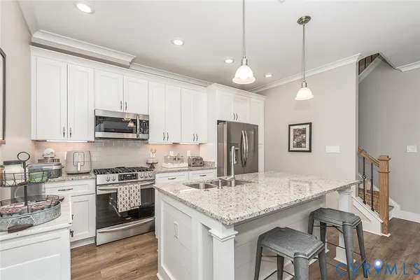 a kitchen with stainless steel appliances granite countertop a sink a stove a refrigerator cabinets and a dining table with wooden floor