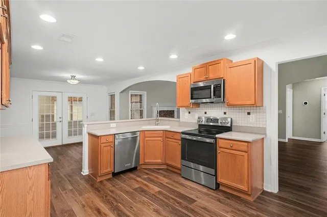 a kitchen with stainless steel appliances granite countertop a stove top oven a sink dishwasher and a refrigerator with wooden floor