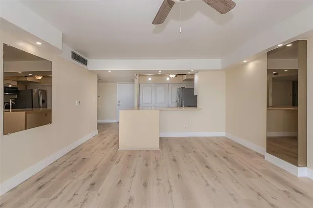a view of an empty room with wooden floor and a ceiling fan
