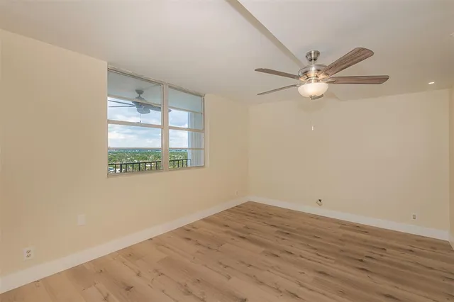 an empty room with wooden floor fan and windows