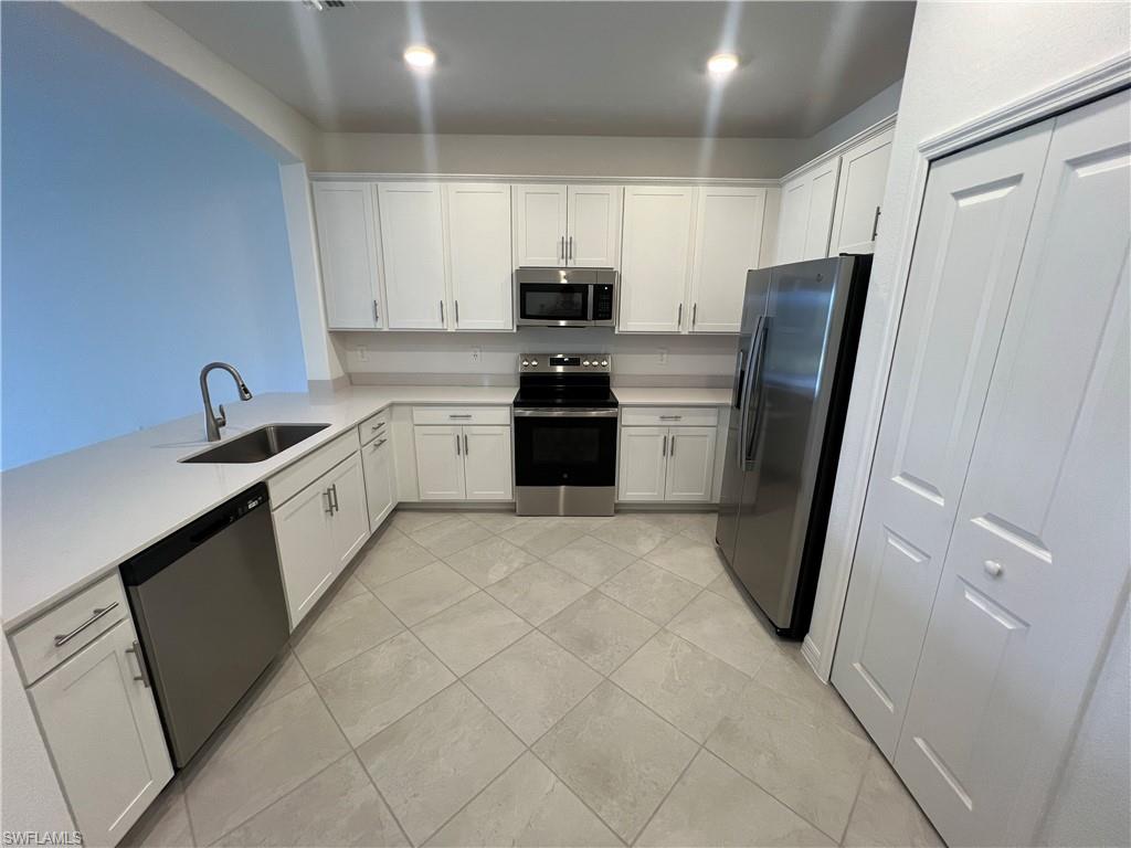 2320 Dragonfruit Way Naples, FL 34120 - Photo 5 of 33 Kitchen featuring white cabinetry, light countertops, stainless steel appliances, a sink, and light tile patterned flooring
