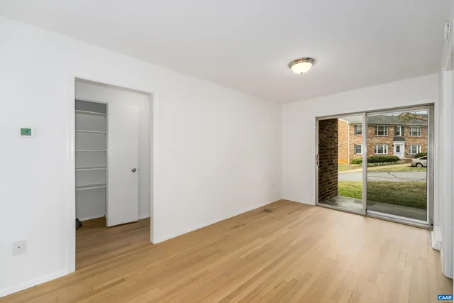 an empty room with wooden floor and way to kitchen