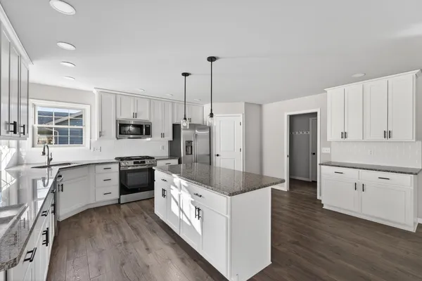 a large kitchen with stainless steel appliances granite countertop a stove a sink dishwasher a refrigerator and white cabinets with wooden floor