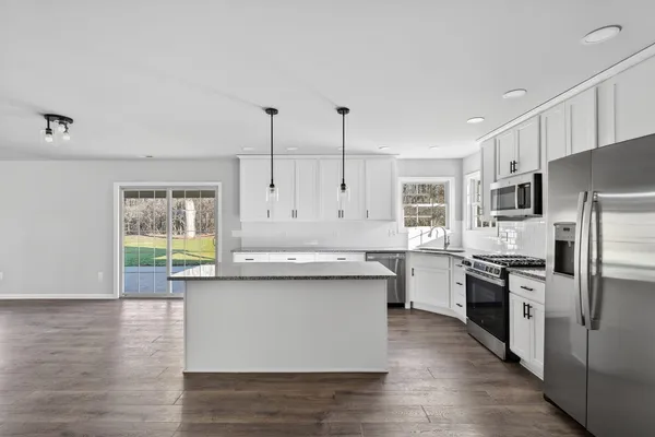 a kitchen with stainless steel appliances granite countertop a stove a sink dishwasher a refrigerator white cabinets and wooden floor next to a window
