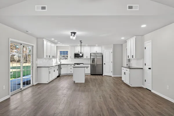 a large white kitchen with a refrigerator a sink dishwasher a stove and white cabinets with wooden floor