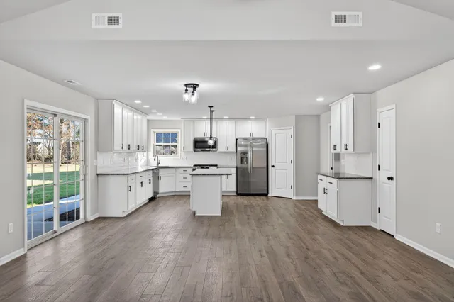 a large white kitchen with a refrigerator a sink dishwasher a stove and white cabinets with wooden floor