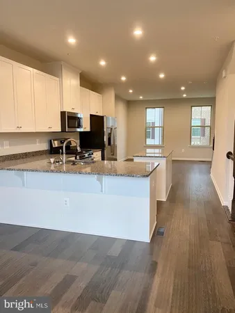a view of kitchen with stainless steel appliances granite countertop a stove a sink a refrigerator and white cabinets with wooden floor