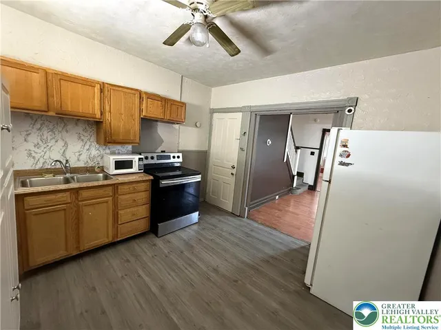 a kitchen with granite countertop a refrigerator a sink dishwasher a stove and white cabinets with wooden floor