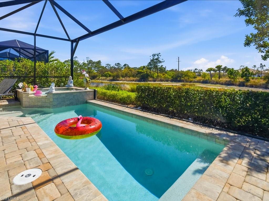 6827 Saona Court Naples, FL 34113 - Photo 17 of 36 a view of a swimming pool with a table and chairs under an umbrella