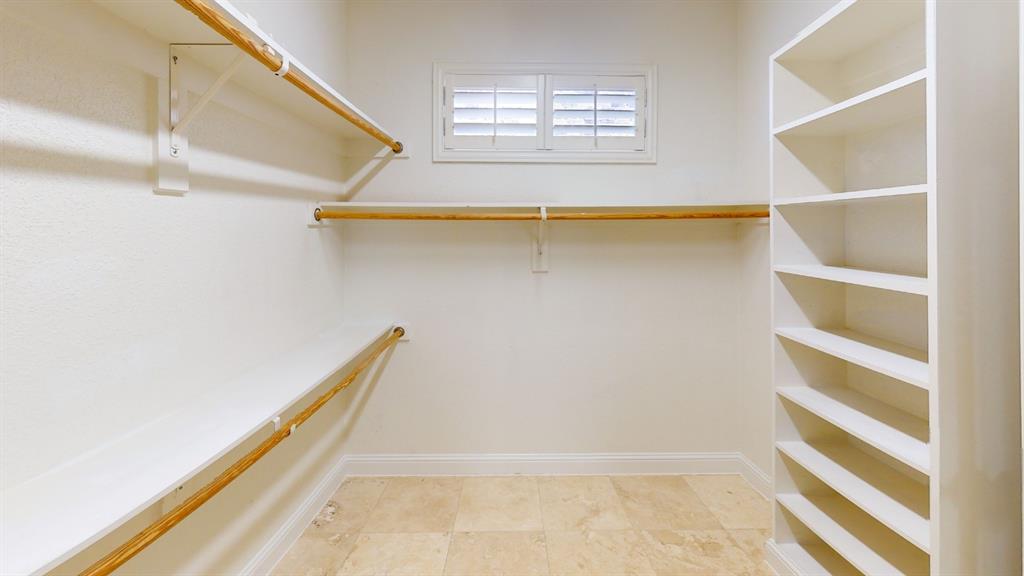4516 Gilbert Avenue Dallas, TX 75219 - Photo 23 of 28 Walk-in closet featuring stone tile flooring, a window with plantation shutters, multiple white shelving units, and ample hanging rods