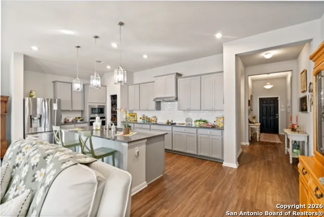 a kitchen with stainless steel appliances kitchen island granite countertop a stove a sink a refrigerator and white cabinets with wooden floor