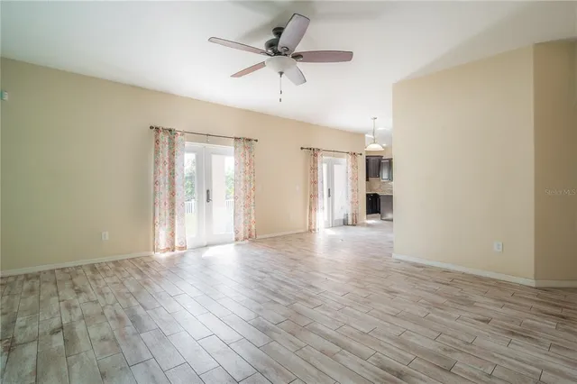 a view of an empty room with wooden floor and a ceiling fan