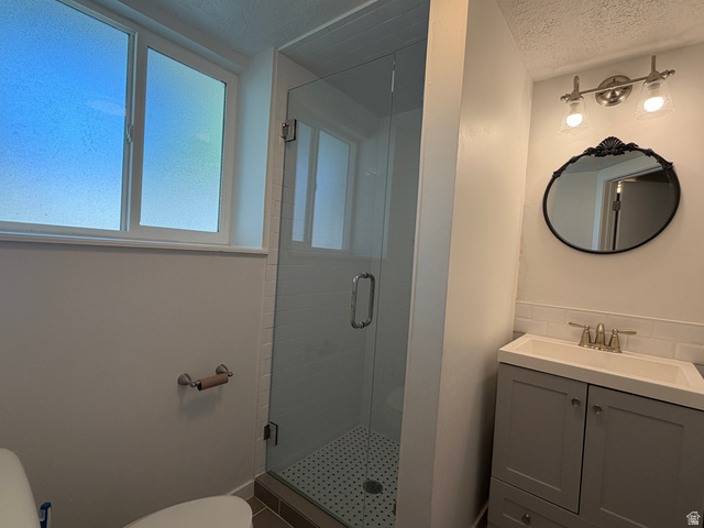375 East 10560 South Sandy, UT 84070 - Photo 15 of 21 Bathroom featuring a glass-enclosed shower, a vanity with under-sink storage, a circular mirror, and a window with frosted panes