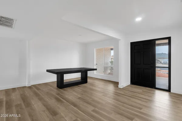 a view of an empty room with wooden floor and kitchen view