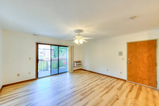 an empty room with wooden floor fan and windows