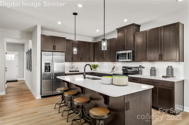 a kitchen with stainless steel appliances kitchen island granite countertop a sink a stove a refrigerator and chairs with wooden floor