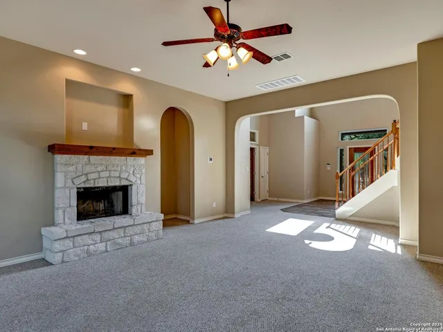 a view of a livingroom with a fireplace a ceiling fan and windows