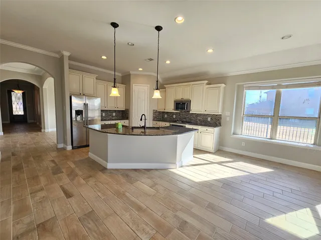 a large kitchen with stainless steel appliances granite countertop a stove a sink dishwasher a refrigerator and white cabinets with wooden floor