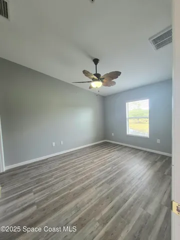 an empty room with wooden floor chandelier fan and windows