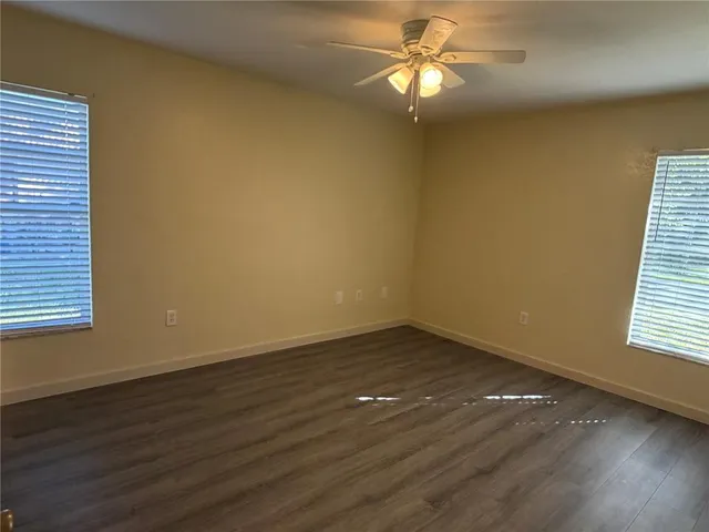 an empty room with wooden floor fan and windows
