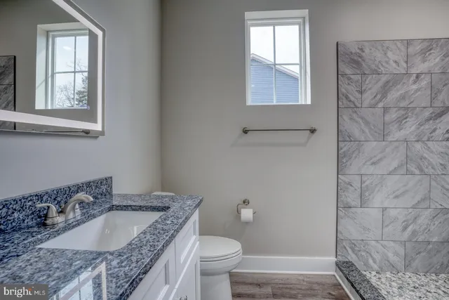 a bathroom with a granite countertop sink a toilet and a window